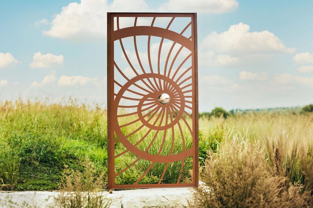 Nahaufnahme der Sichtschutzwand - Spirale, gefertigt aus robustem Metall mit Edelrost Patina. Die spiralförmige Gestaltung und die Edelstahlkugel verleihen der Wand sowohl ästhetische Eleganz als auch Funktionalität, perfekt für Sichtschutz und als Rankhilfe im Garten